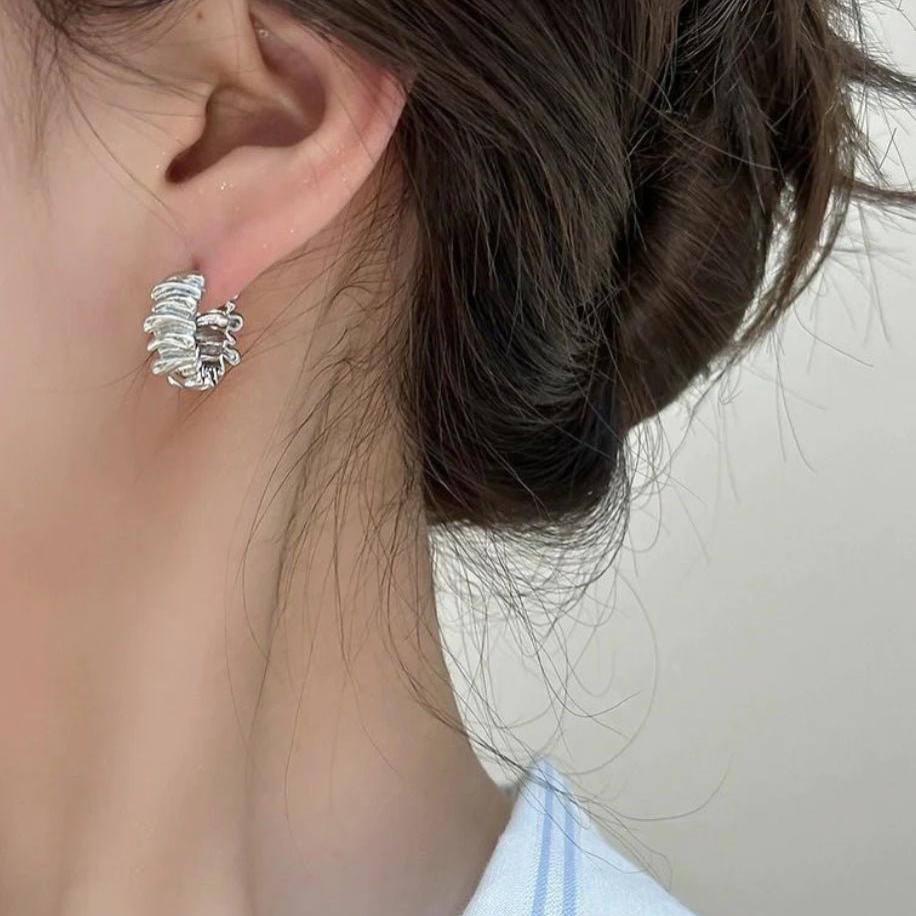 Model wearing silver folded and textured squiggle hoops